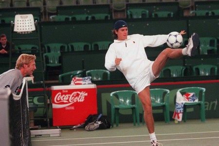 A tennis player kicking a soccer ball.