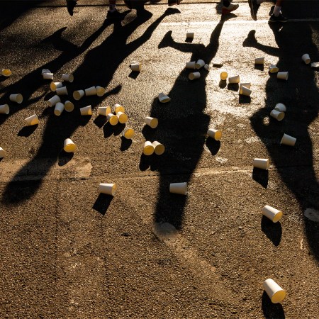 A bunch of marathon cups on the concrete, with runners' shadows in the background.