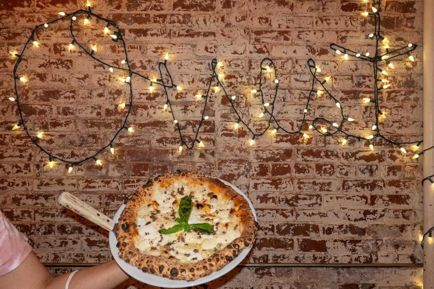 hand holding white pizza, light up sign on brick wall