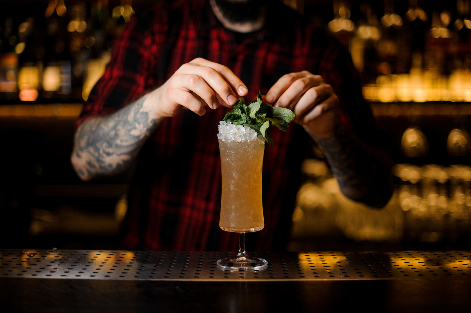 Barman decorating tasty Sherry Cobbler drink in a cocktail glass with mint leaves on the bar counter