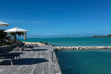 an ocean pool with blue skies and a grey wooden deck with chairs and white umbrellas