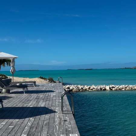 an ocean pool with blue skies and a grey wooden deck with chairs and white umbrellas