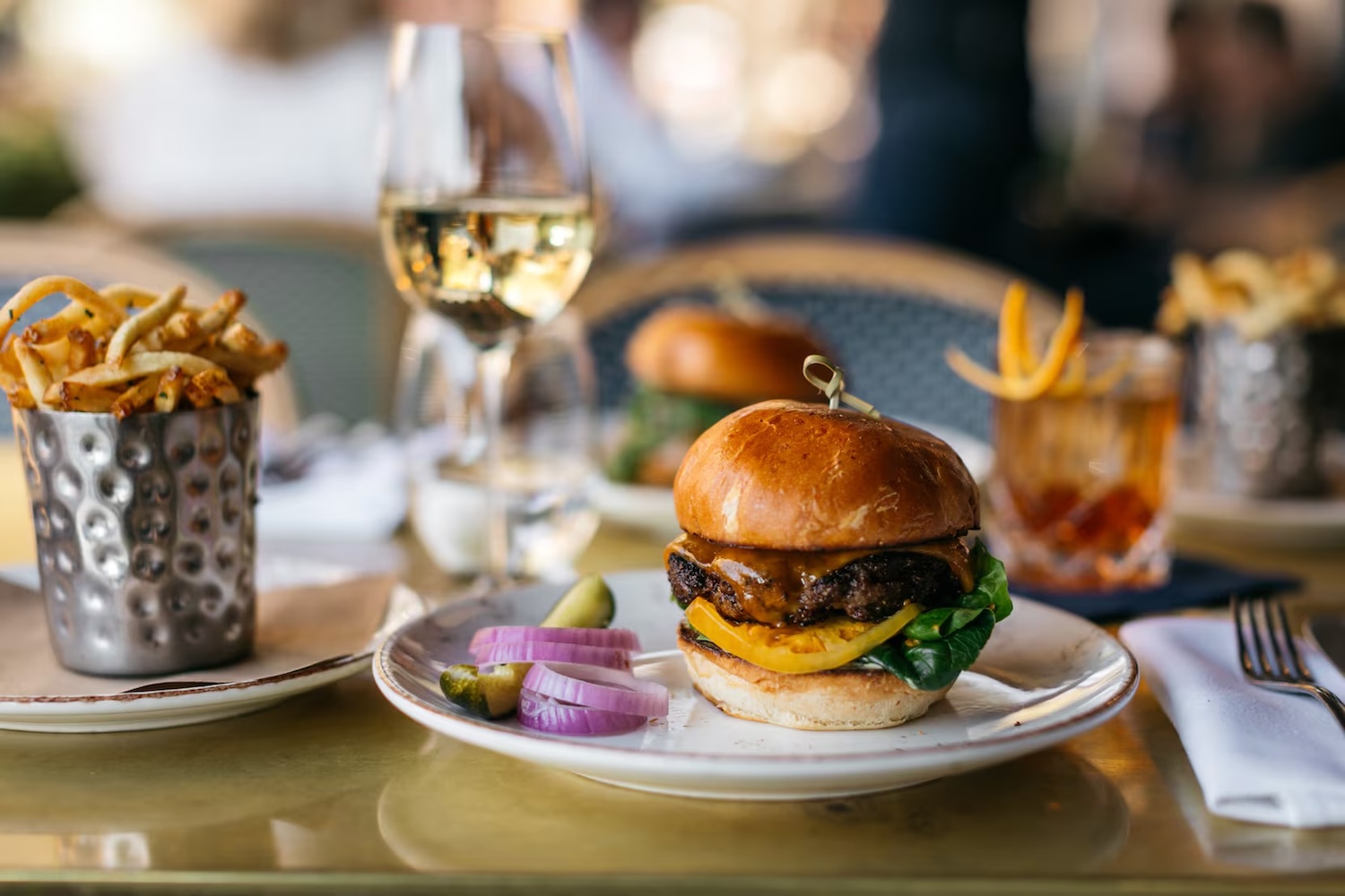 burger with a side of onions and a pickle, wine in a glass