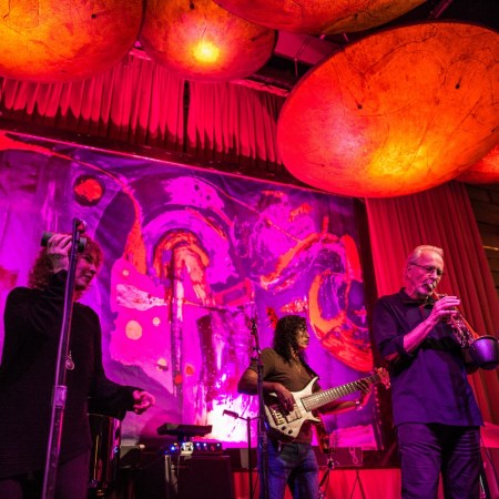 man playing trumpet and others playing instruments on stage, pink and red lights