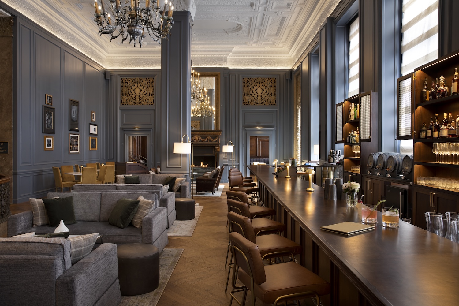 gray couches and walls, wooden stools, bar, paintings on wall, candelabra hanging from ceiling