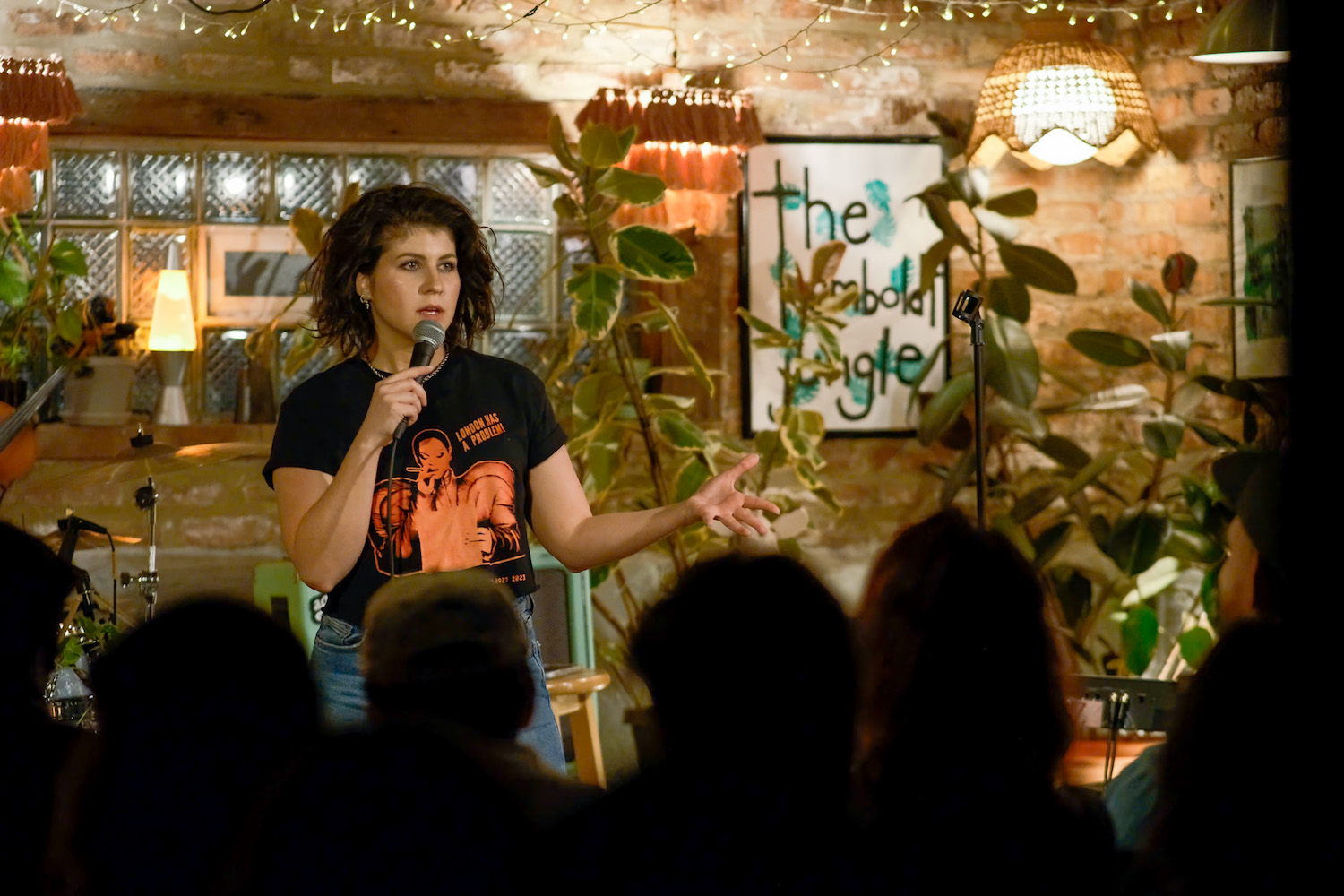 A woman stands on a stage with a microphone in front of a crowd.