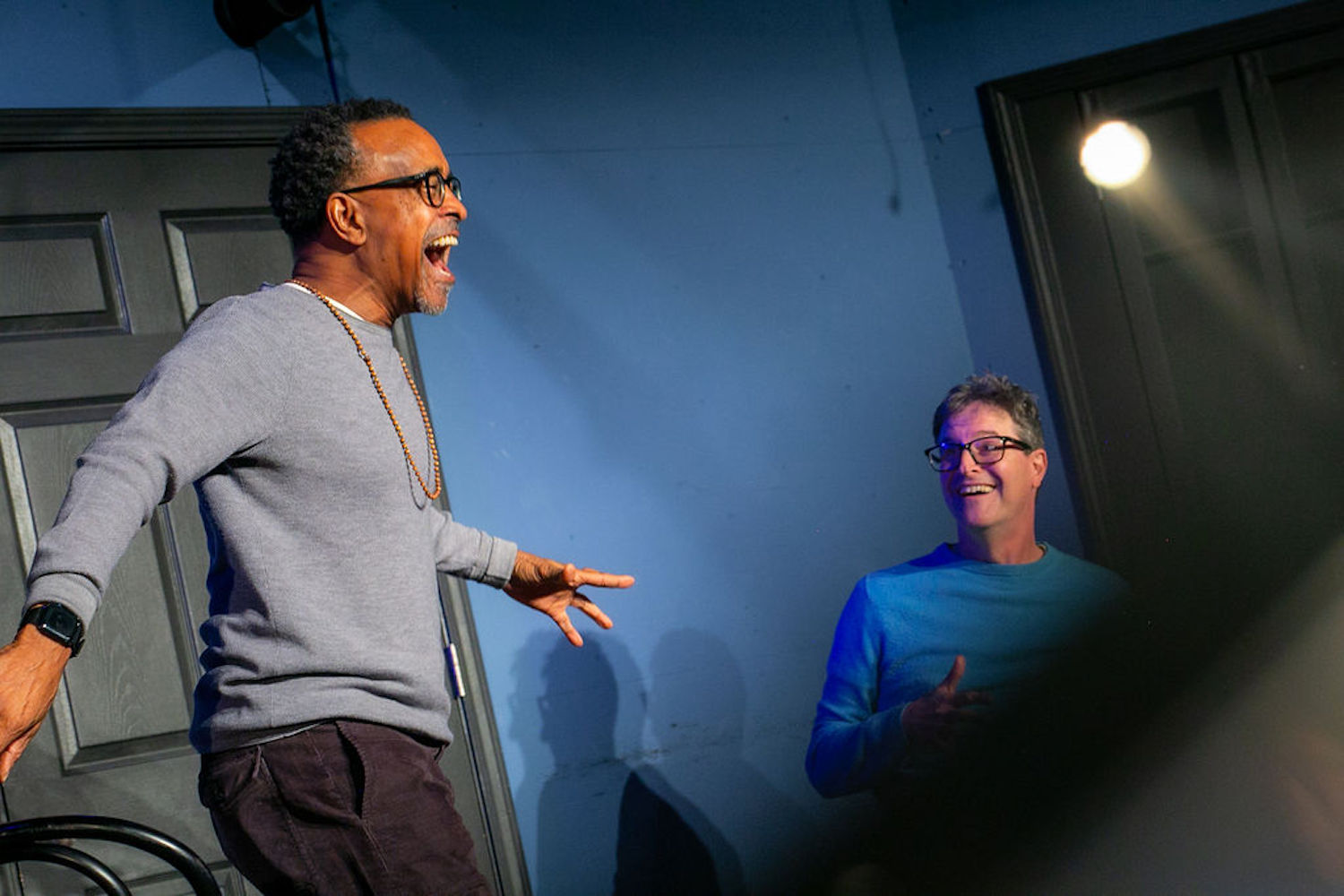 Two men perform on a stage in front of a blue background.