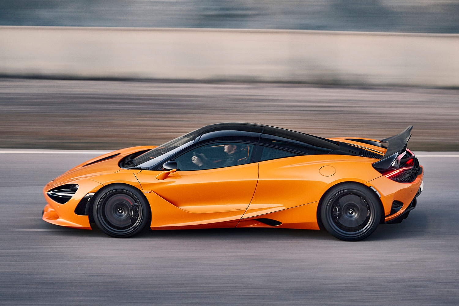 An orange McLaren supercar driving down the road