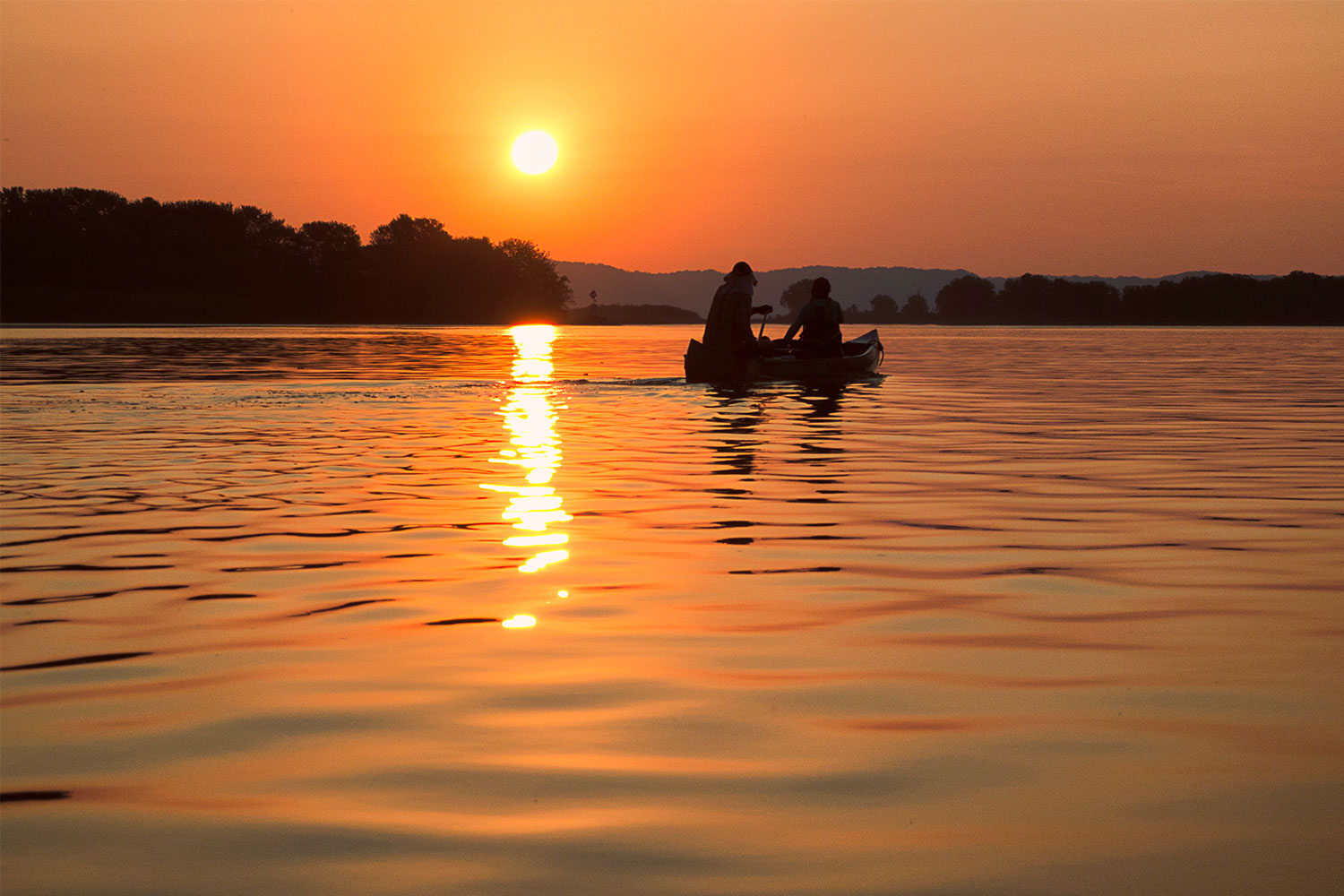 Two paddlers in a canoe on the Mississippi River at sunset, by Domonick Zanarini
