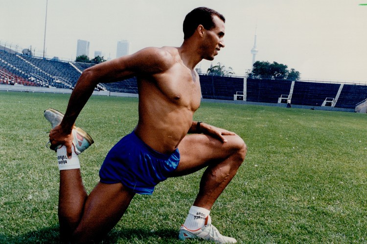 A fit man stretching on a turf field without a shirt