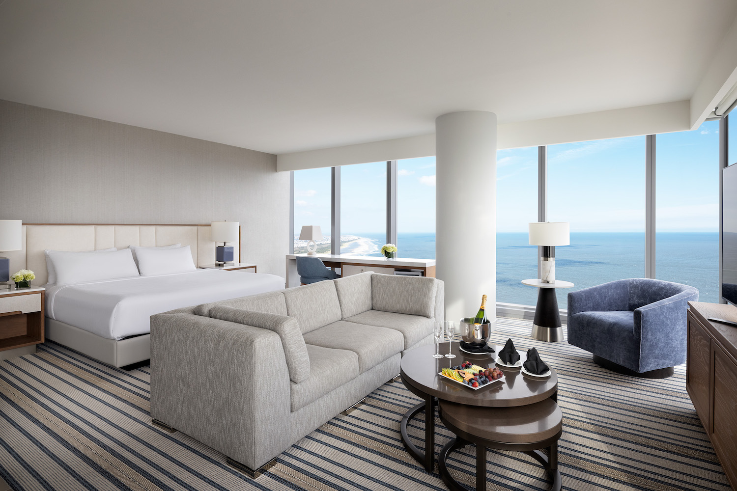 a hotel room with a bed, couch and floor-to-ceiling windows overlooking the ocean