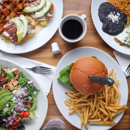 a brunch spread with eggs, potatoes, a cobb salad, burger, fruit salad and coffees
