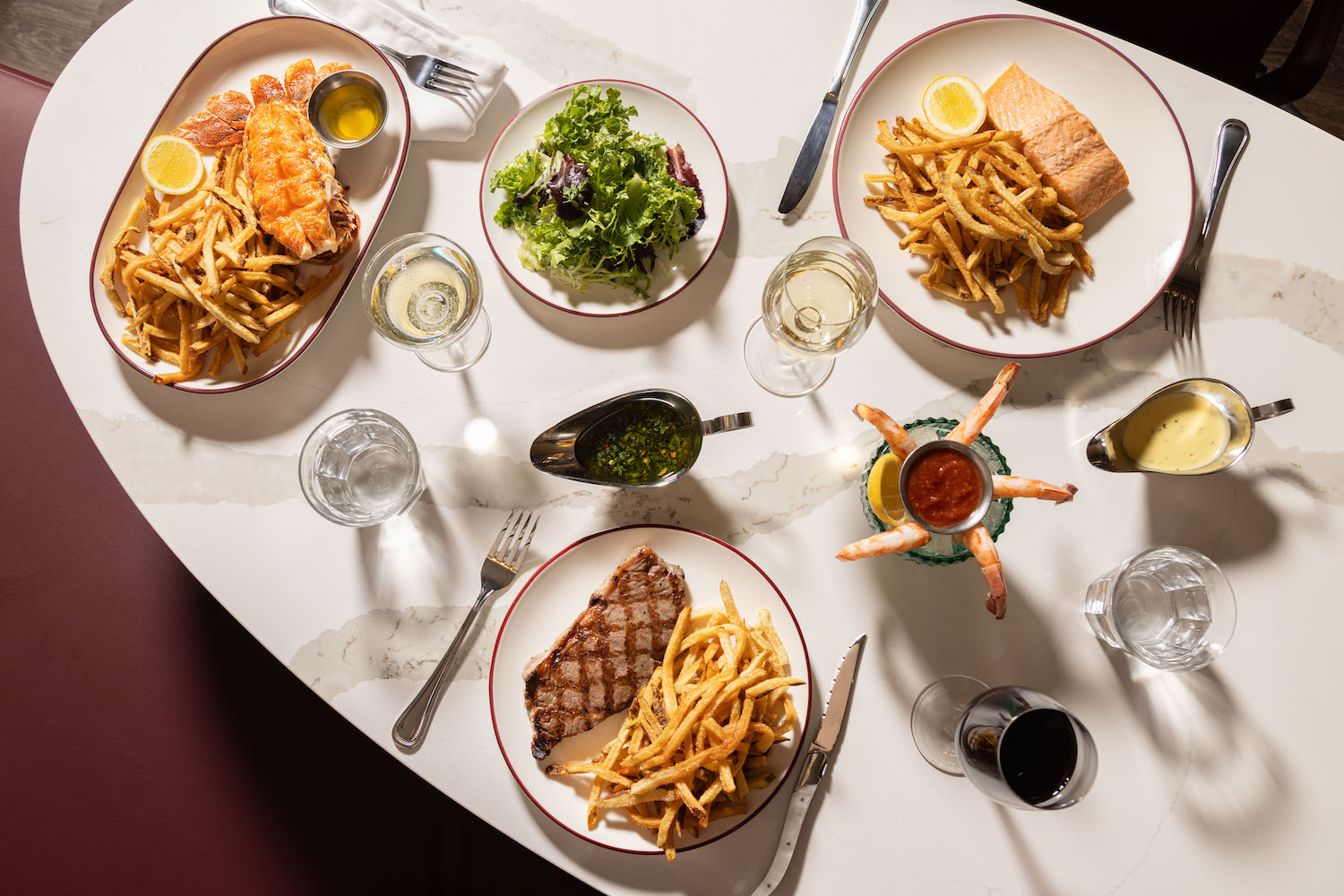 a white table laid with lobster, salmon, steak, french fries, shrimp cocktail and salad