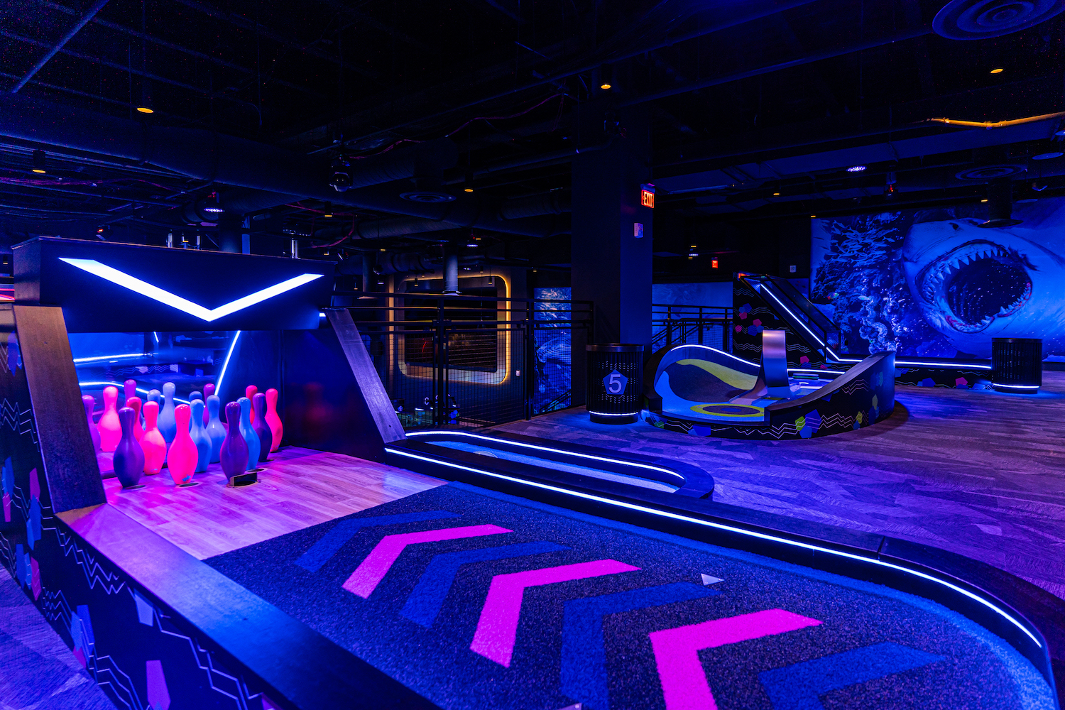 a mini golf course illuminated with black lights and a hole that looks like a mini bowling alley