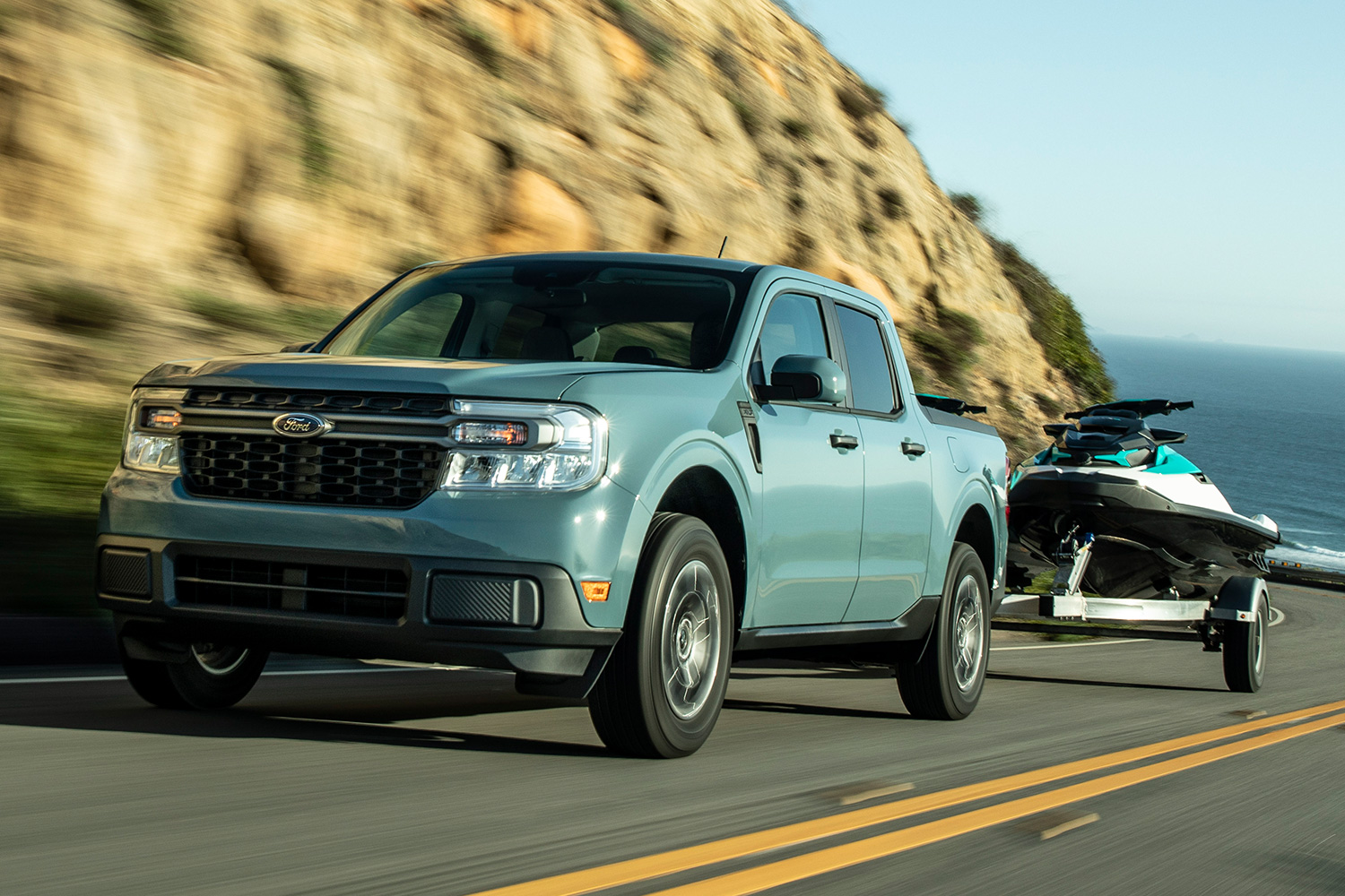 Ford Maverick Hybrid XLT towing a jet ski up a road next to the ocean
