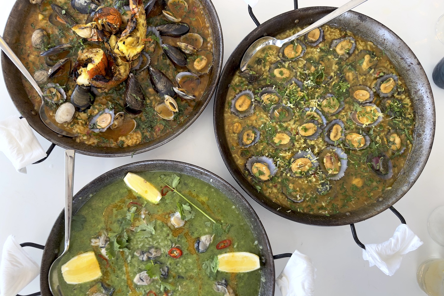 3 paella pans with three different types of seafood rice