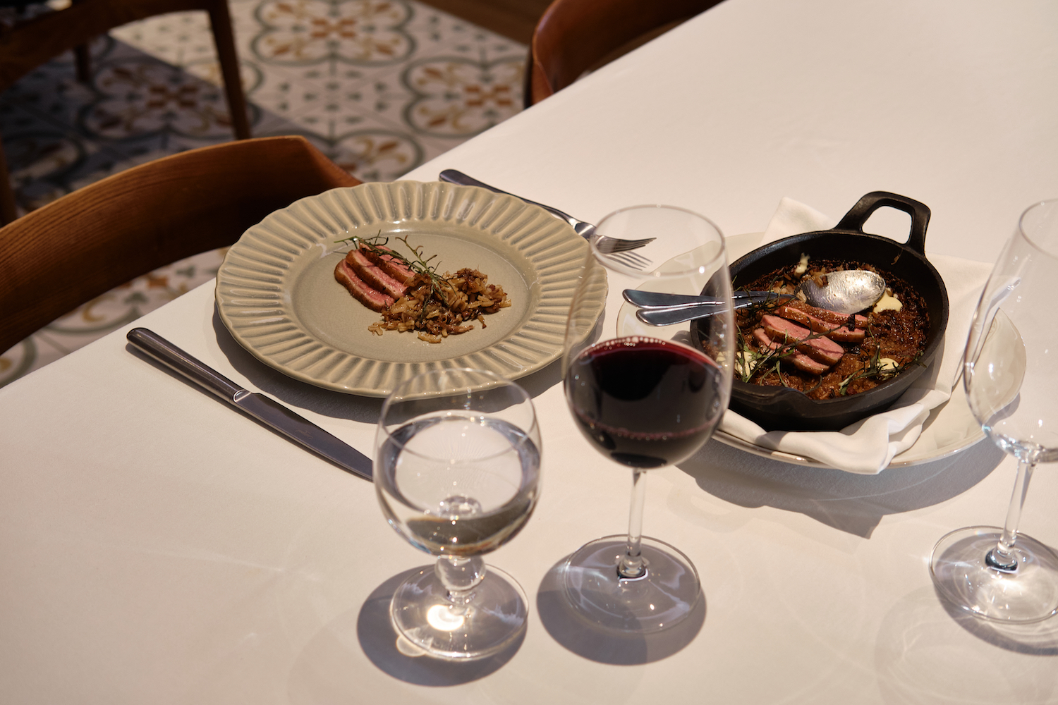 a plate of roasted duck rice next to a cast iron dish of roasted duck rice with red wine and water on a white tablecloth