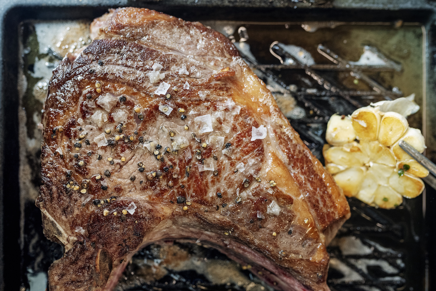 A tomahawk steak finished with Maldon next to a roasted head of garlic