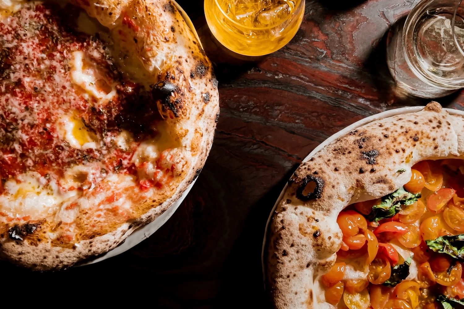 two pizzas on a wooden table with beverages in glass goblets