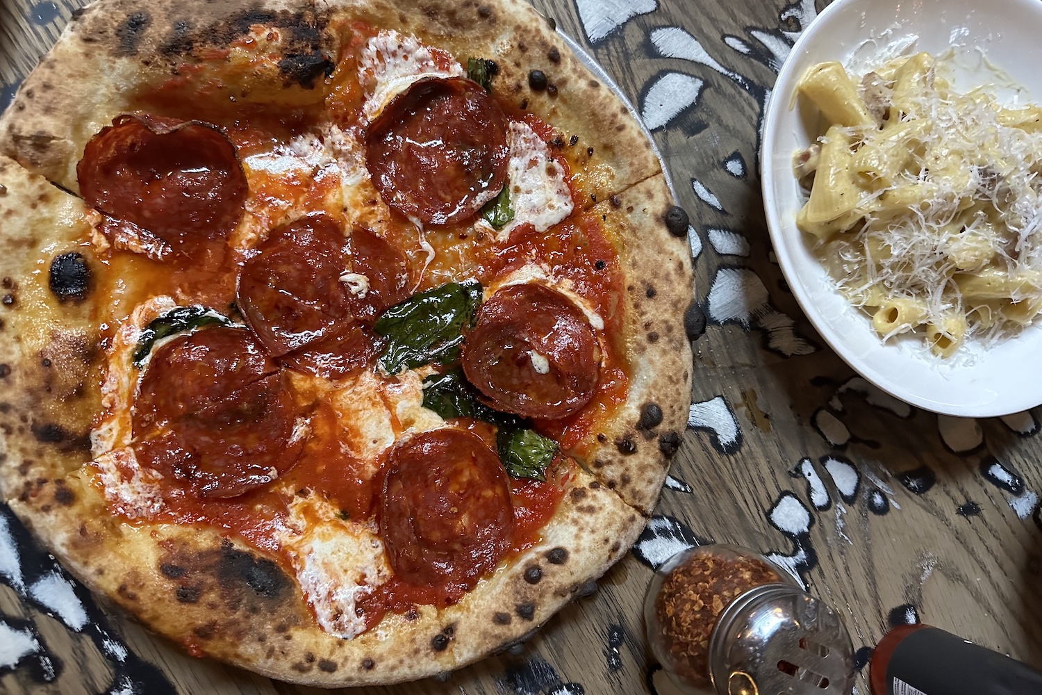 a pepperoni pizza and pasta in a white bowl on a wooden table