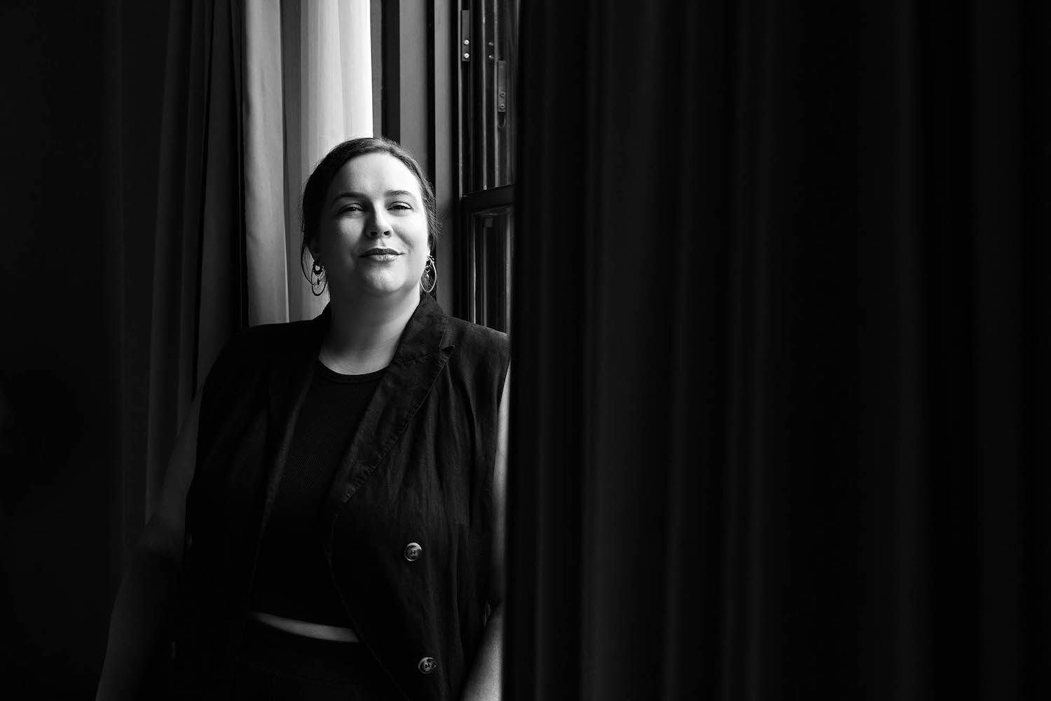 a photo of a woman standing against a window in black and white