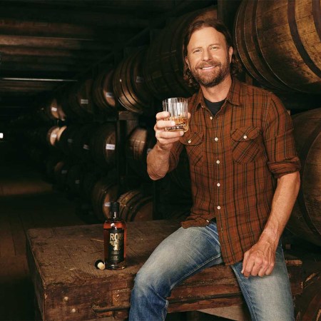Dierks Bentley holding a glass of whiskey in a rickhouse