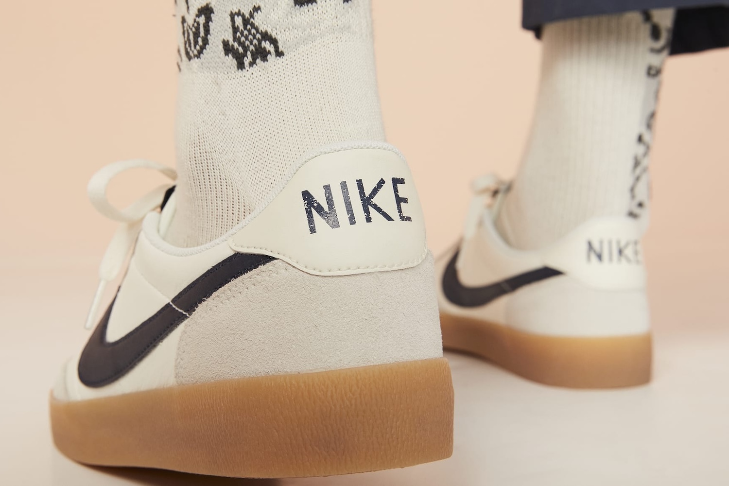 A man wearing grey, white and tan Nike sneakers seen from the back with the word "NIKE" emblazoned on the heel
