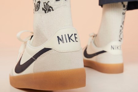 A man wearing grey, white and tan Nike sneakers seen from the back with the word "NIKE" emblazoned on the heel