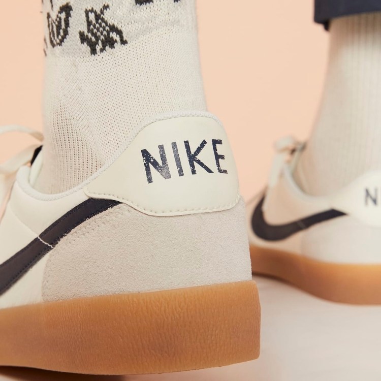 A man wearing grey, white and tan Nike sneakers seen from the back with the word "NIKE" emblazoned on the heel