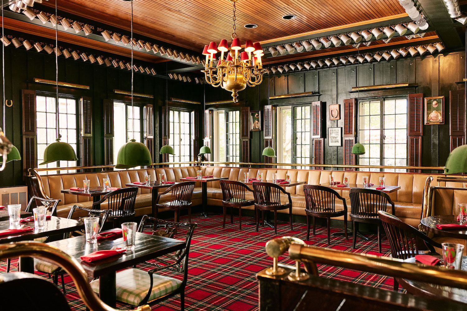 a dining room with red plaid carpet, green equestrian helmet lamps and lots of dark wood