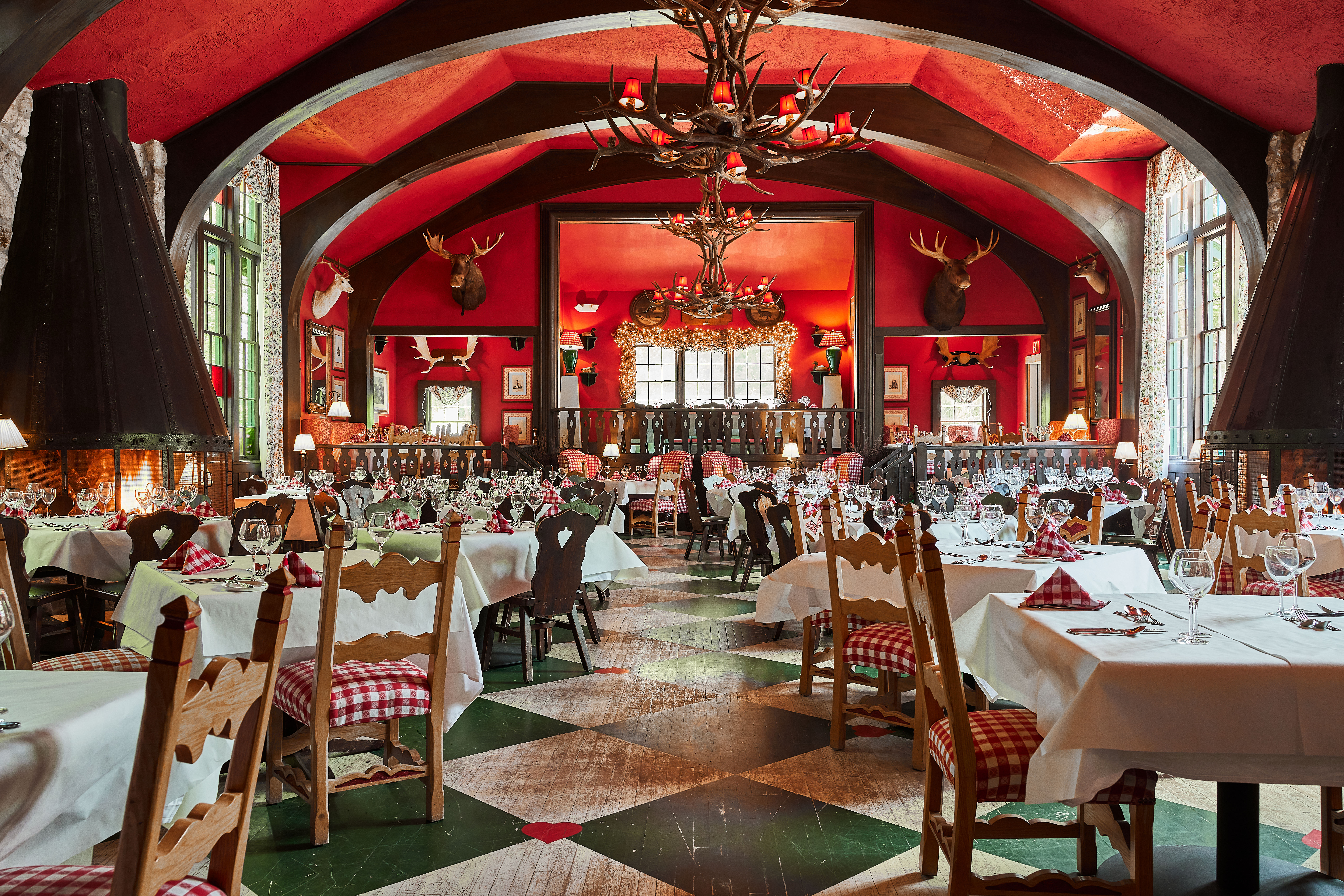 a restaurant with high ceilings, antler chandeliers, red and white checkered linens