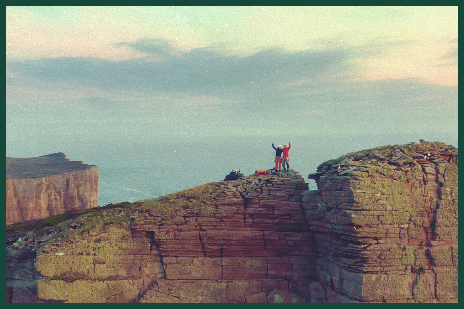 Jesse and Molly Dufton standing atop the sea stack, their arms raised in triumph.