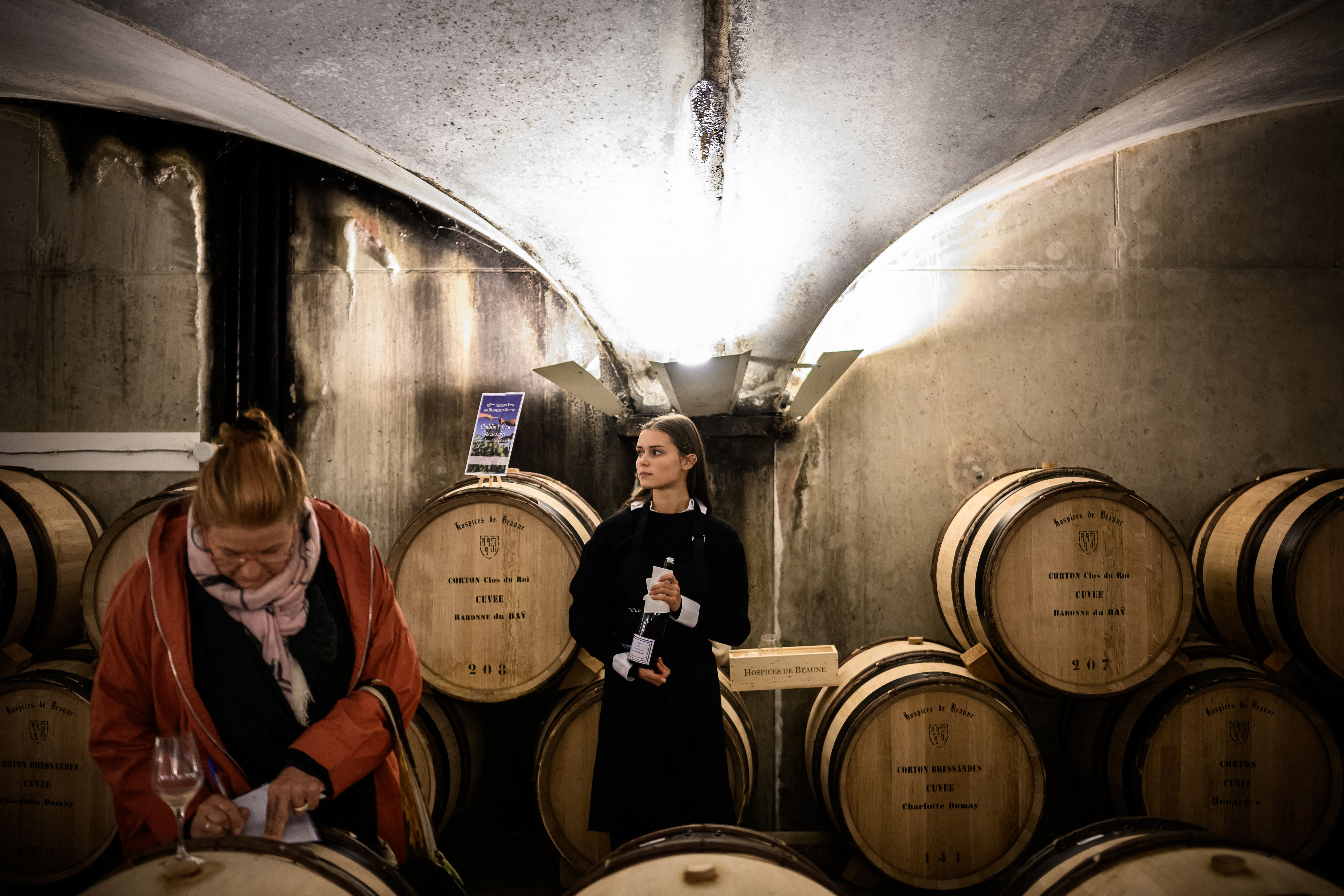 A wine worker waits in front of wine barrels in the "Nouvelle cuverie" (new wine tank room) to serve wine to people who come to taste the wines that will be sold during 162nd edition of the "Hospices de Beaune" charity auction wine sale, in Beaune, central France, on November 20, 2022. - The annual wine auction finances the Hospices' Museum as well as other hospital activities. (Photo by JEFF PACHOUD / AFP) (Photo by JEFF PACHOUD/AFP via Getty Images)