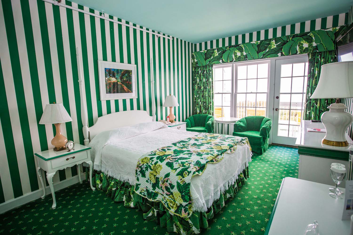 a hotel room with green and white striped walls, green carpet and palm leaf accents