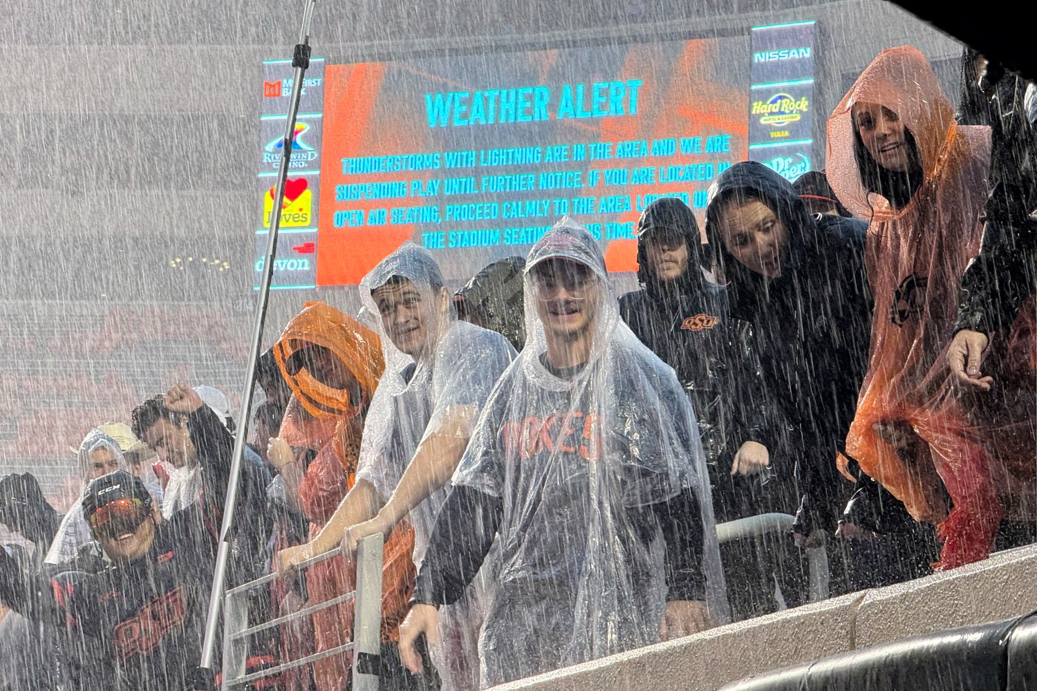 College football fans in the rain. A recent NCAA agreement allowing schools to directly pay student athletes may increase prices for fans.
