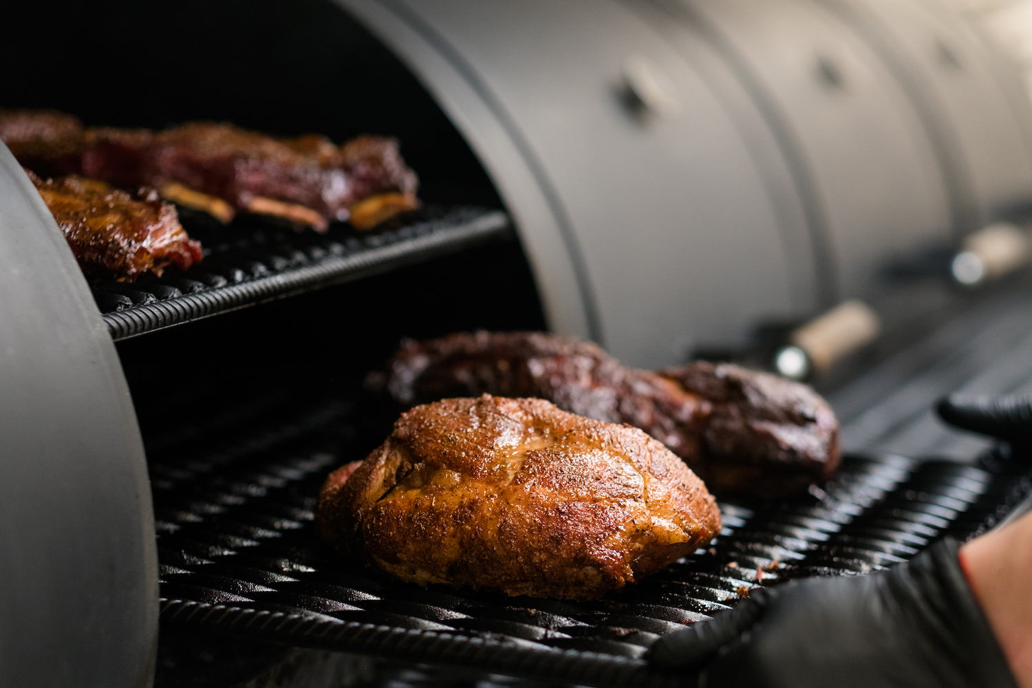Closeup of chef cooking poultry, beef and pork meat, ribs in BBQ smoker