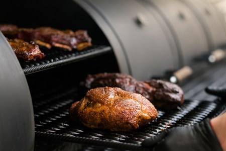Closeup of chef cooking poultry, beef and pork meat, ribs in BBQ smoker
