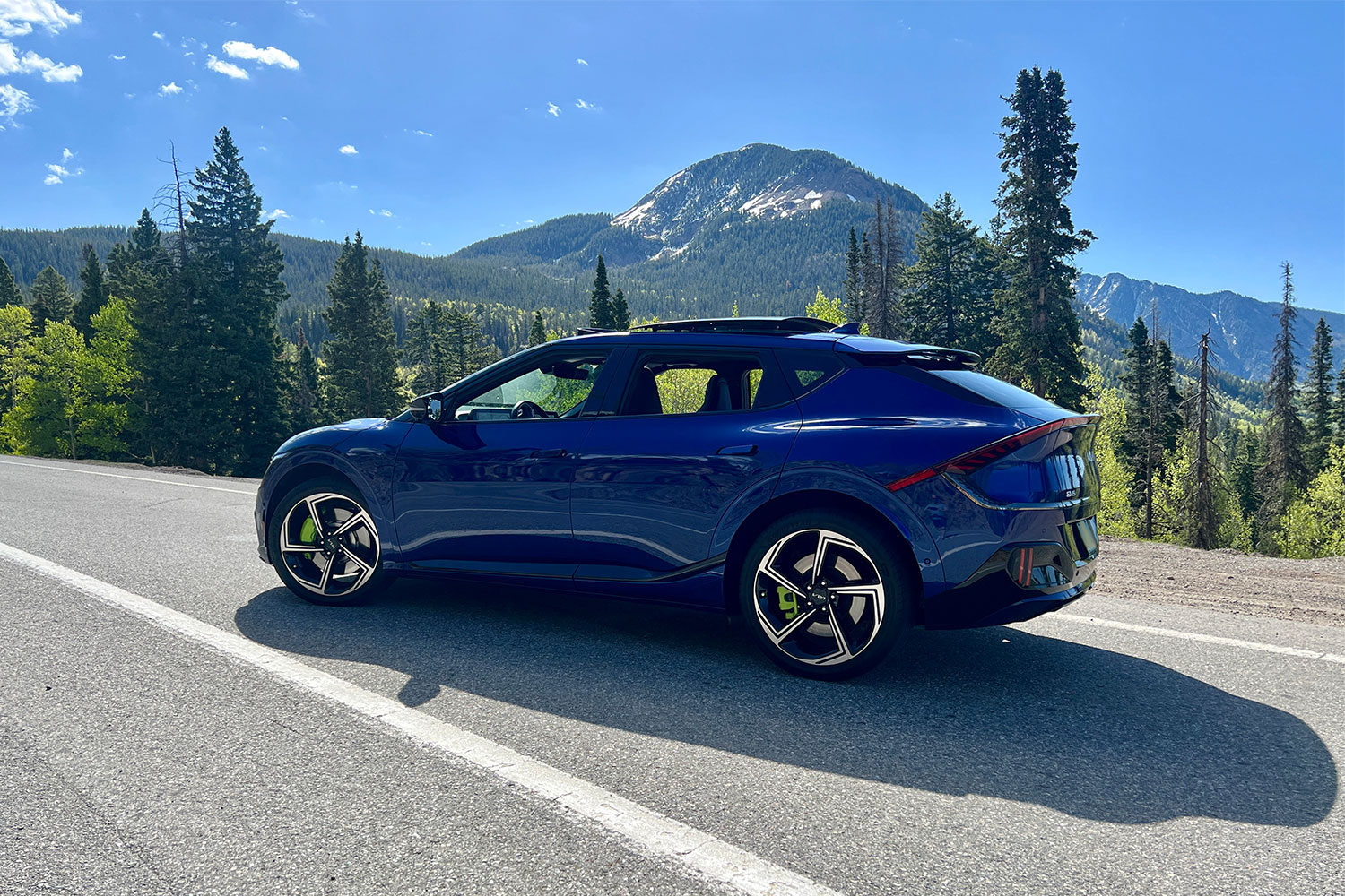 A blue Kia EV6 sitting on the side of the road with a mountain in the background