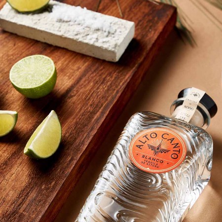 Alto Canto blanco tequila near salt and limes on a table