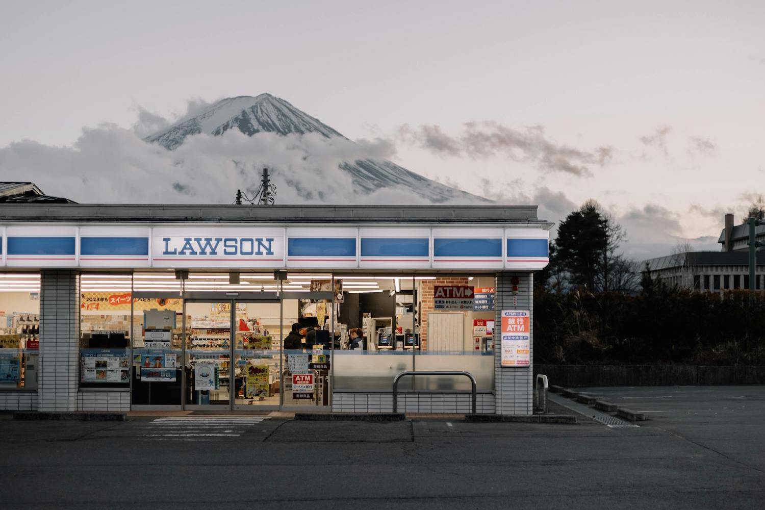 a japanese lawson konbini at dusk in front of a snow-covered mountain