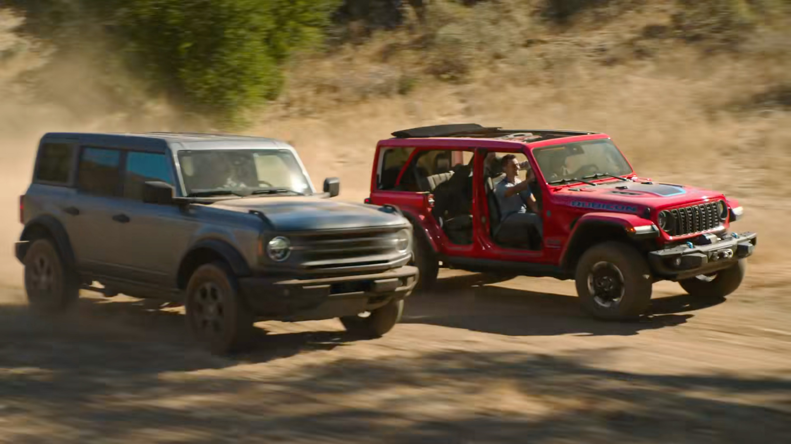 A Jeep Wrangler Rubicon 4xe driving past a Ford Bronco in the Jeep Super Bowl 59 ad from 2025 called "Owner's Manual"