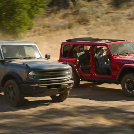 A Jeep Wrangler Rubicon 4xe driving past a Ford Bronco in the Jeep Super Bowl 59 ad from 2025 called "Owner's Manual"