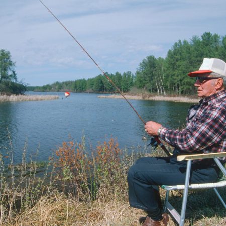 A retiree sitting in a chair, fishing on a lake.