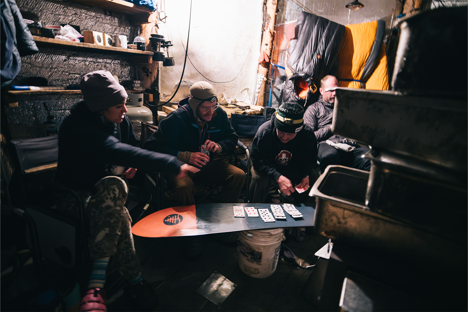 A group of skiers gathered around a snowboard on the inside of a yurt, playing cards.