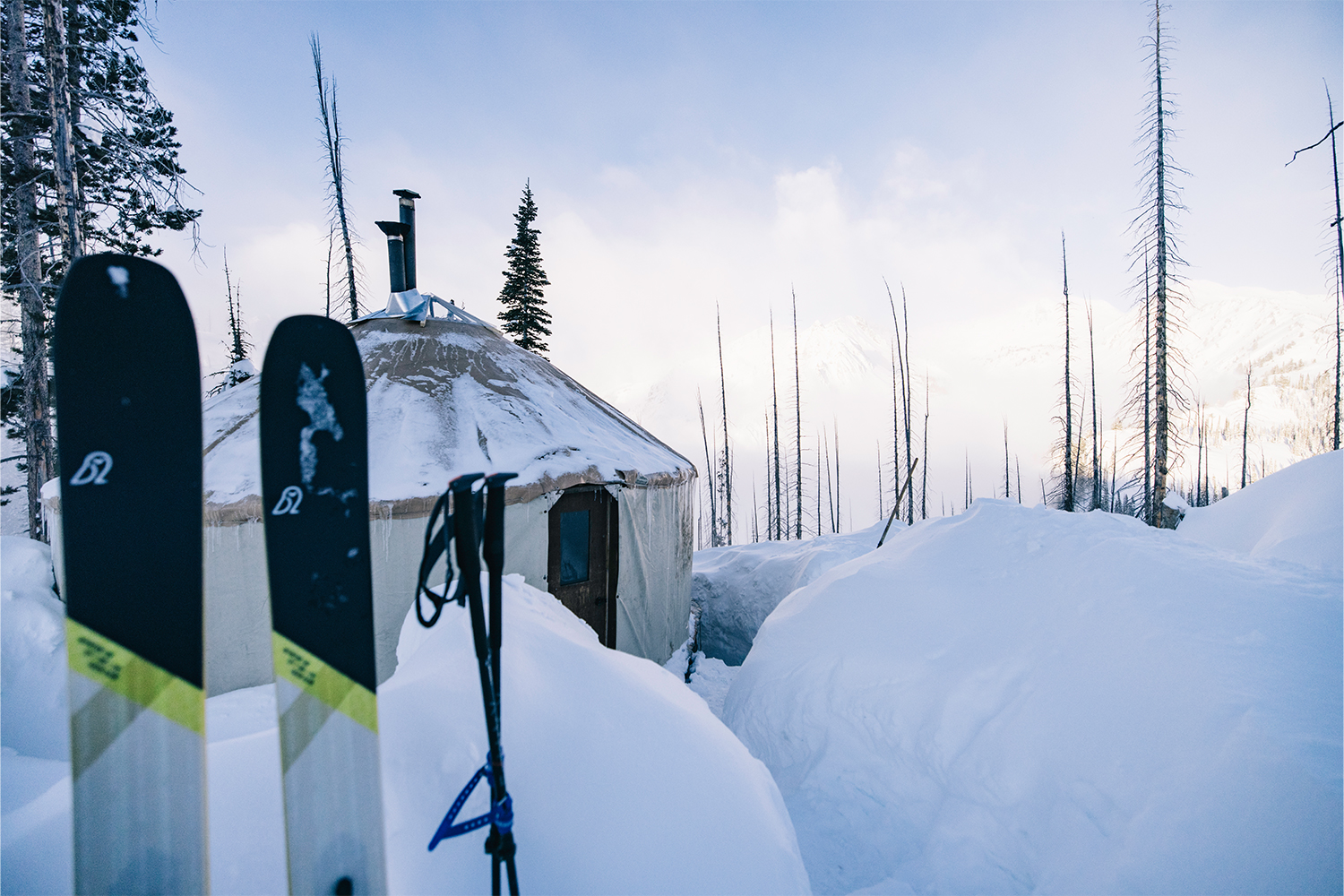 Skis planted in the snow in the foreground, a wintry yurt in the background.