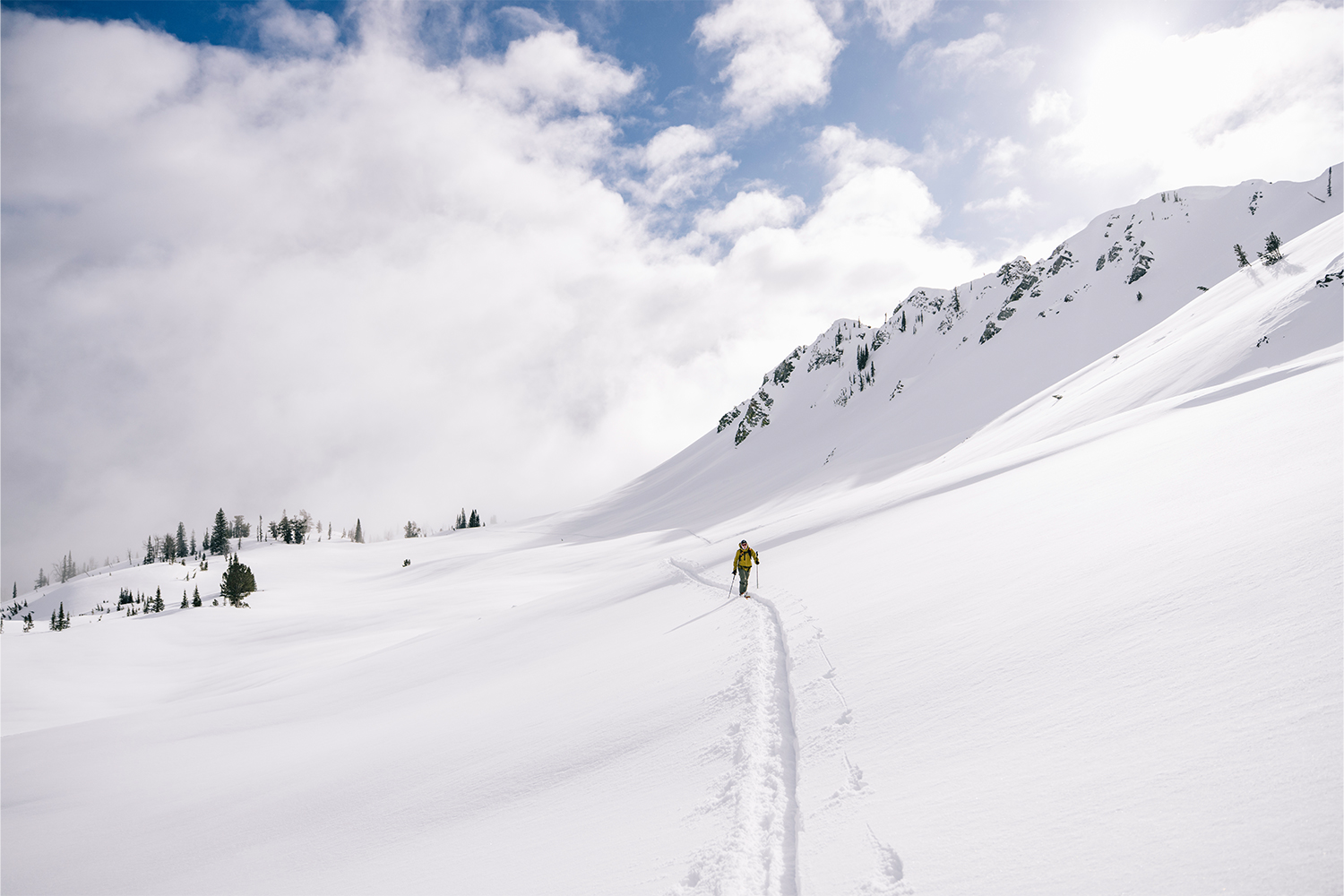 A lone skier walks through pristine snow with mountains beyond them.