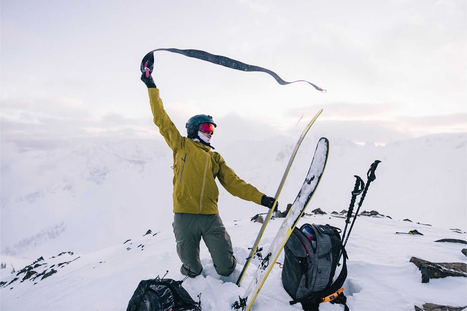 A skier at the top of the mountain, brandishing a ribbon.