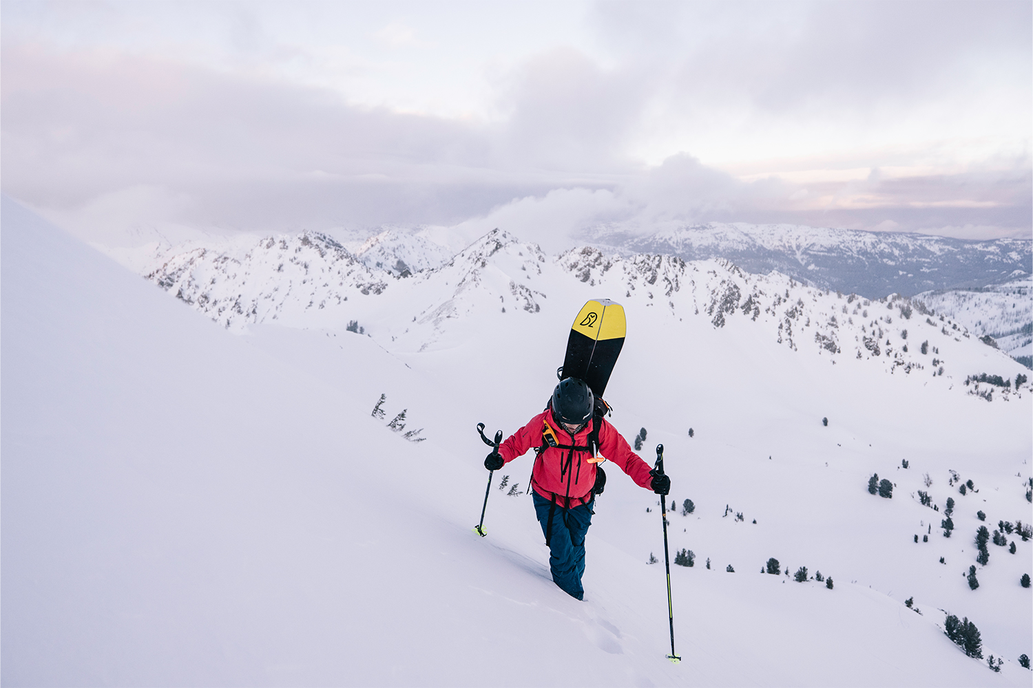 A snowboarder uses her poles to reach the top of the mountain.