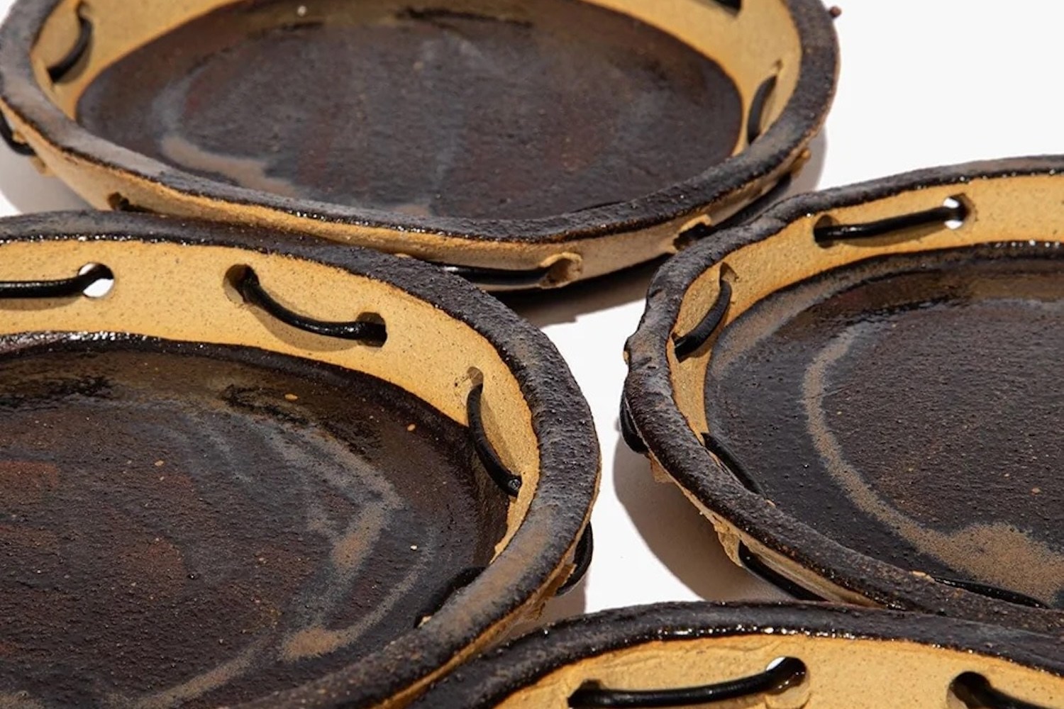 Close-up of several dark brown ceramic bowls with light brown rims and black cords threaded through holes.