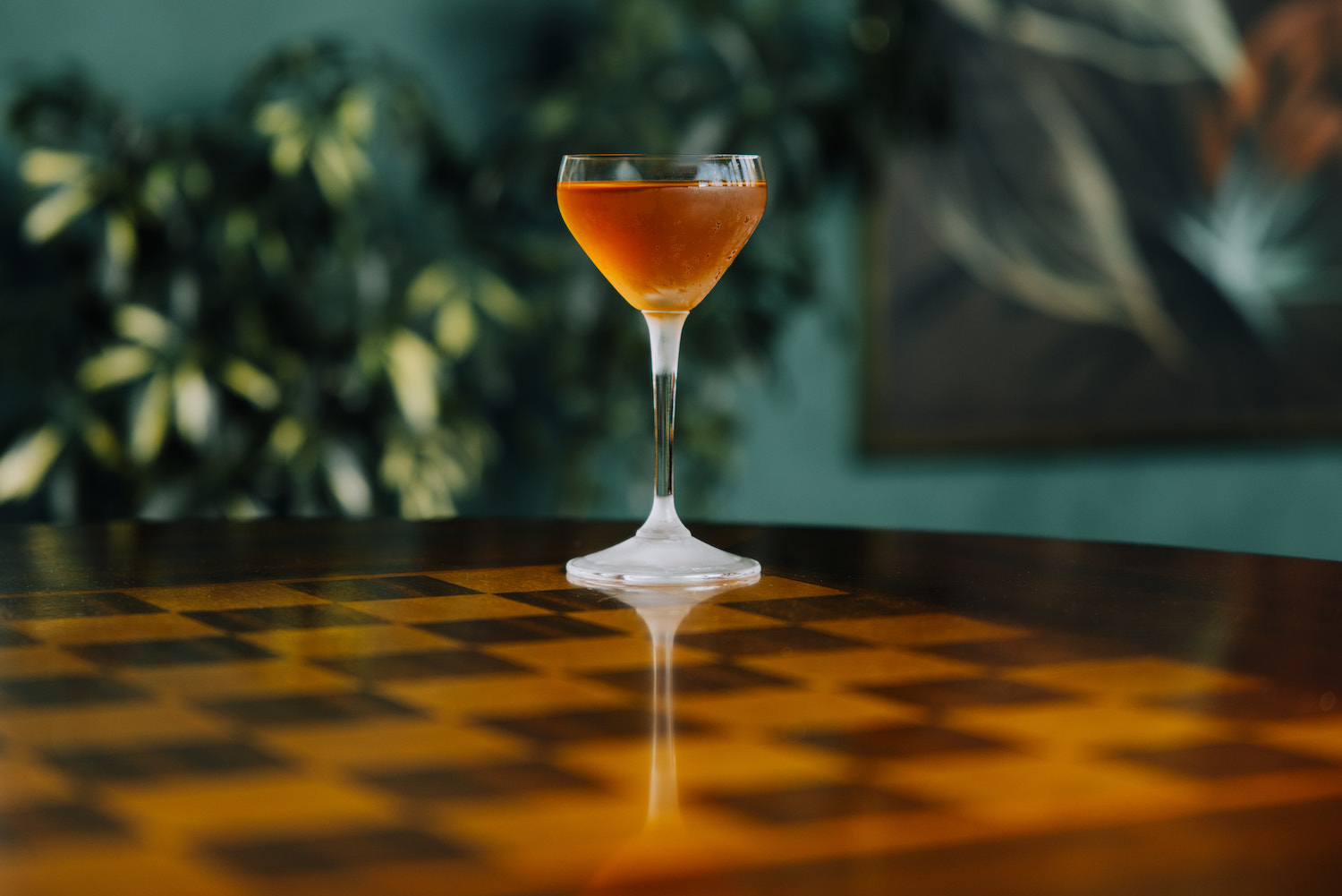 an orange cocktail in a nick and nora glass sitting on a chess board table top
